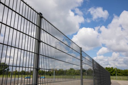Une image en perspective d'une clôture à panneaux. En arrière-plan, ciel bleu avec nuages blancs et pelouses vertes.