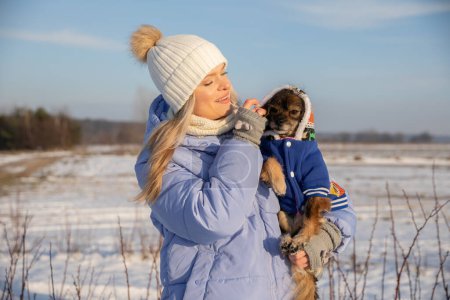 Téléchargez les photos : Une femme est sortie se promener avec son chien. Pendant la promenade, le chien s'est fatigué et ses pattes ont gelé, car il neigeait. La propriétaire a dû prendre son chien dans ses bras. - en image libre de droit