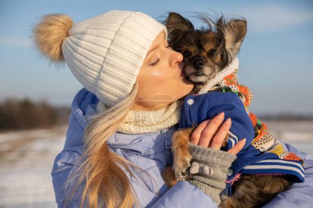 Téléchargez les photos : Gros plan d'une femme blonde embrassant son chien. La femme et le chien sont dehors un jour d'hiver. Les deux sont vêtus de manteaux chauds. - en image libre de droit