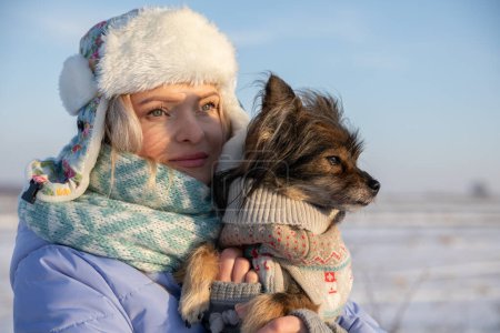 Téléchargez les photos : La propriétaire habillait son chien de vêtements spéciaux pour chien afin de l'empêcher de se refroidir dehors. Une promenade hivernale avec le chien. Un voyage dans le désert. - en image libre de droit