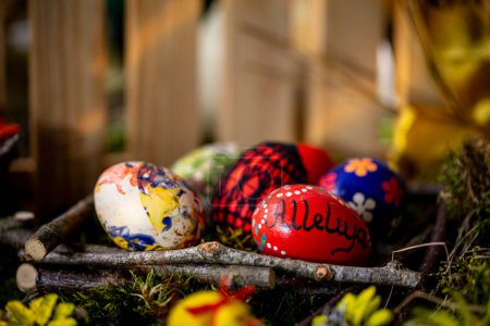 Photo for In this tranquil Easter scene, delicate handcrafted eggs rest in a basket lined with arranged twigs and lush green moss. One egg bears the inscription ,Alleluja, while the others feature floral - Royalty Free Image