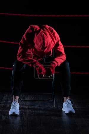 A lost fight of a strong player. He is sitting in a chair. Right after losing the fight. Sad woman after a fight in the ring. In a hoodie.