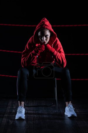A lost fight of a strong player. He is sitting in a chair. Right after losing the fight. Sad woman after a fight in the ring. In a hoodie.