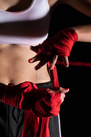 Téléchargez les photos : Une femme se prépare à un combat, enveloppant ses mains dans un bandage de boxe spécial. Une femme forte. L'inévitable combat sur le ring. - en image libre de droit