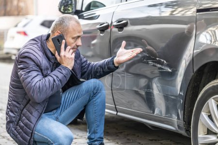 Téléchargez les photos : Un homme appelle la compagnie d'assurance à cause de la porte endommagée de sa voiture parce que le coupable de l'accident s'est enfui du parking. - en image libre de droit