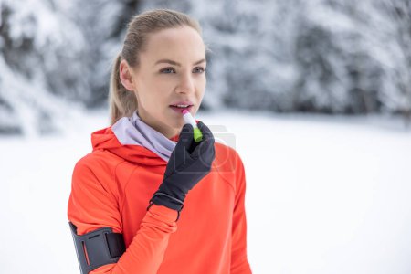 A young female runner applies protective balm to her lips due to the frosty weather, prevention of chapped and dry lips.