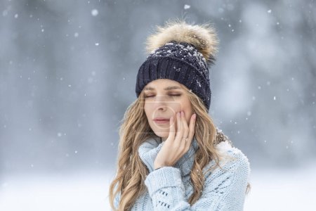 A young woman has a toothache outside in winter weather, she has sensitive enamel to the cold.