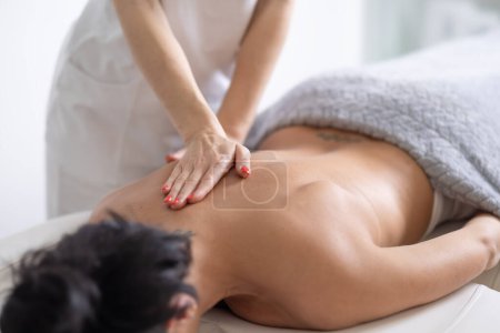 Detail of a masseuse providing a massage to a female client on her sholder blade.
