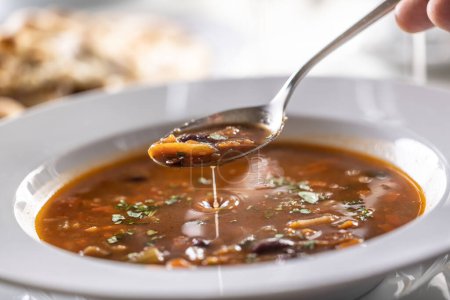 Detail eines Löffels Minestrone-Suppe über dem vollen Teller.