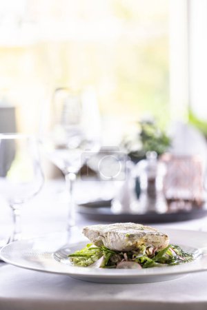 Téléchargez les photos : Cog fish avec salade verte et sauce balsamique est servi sur une table avec fond blanc. - en image libre de droit