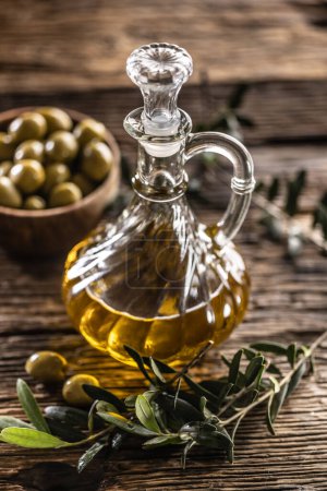 Foto de El aceite de oliva transparente y dorado está diseñado con aceitunas en cuenco de madera y hojas de aceitunas.. - Imagen libre de derechos