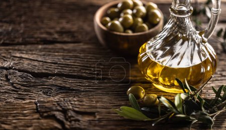 Photo for Glass bottle of olive oil and leaves with olives are designed on wooden table. - Royalty Free Image
