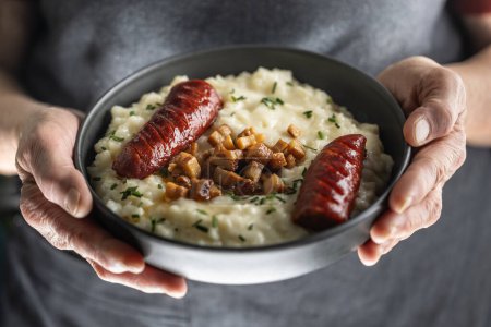 Las manos de un cocinero casero mayor sostienen un plato con un plato nacional eslovaco - Bryndzove Halusky.