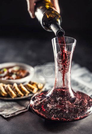 Foto de El vino tinto se vierte de una botella en una jarra sobre una mesa en la que hay gulash de venado, húngaro o vienés con albóndigas de Karlovy Vary.. - Imagen libre de derechos