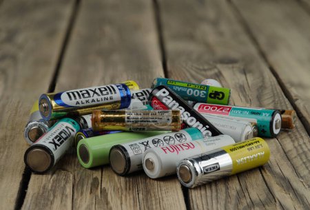 Photo for Kyiv, Ukraine - May 20, 2023: A pile of used and damaged batteries from various manufacturers lies on a wooden texture. Selective focus. - Royalty Free Image