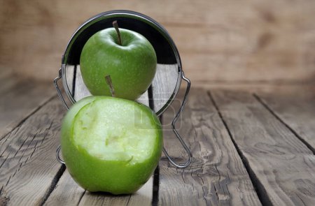 Ein angebissener grüner Apfel spiegelt sich mit seiner schönen unversehrten Seite im Spiegel. Zwei Gesichtspunkte. Selektiver Fokus.  