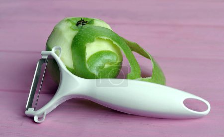 Téléchargez les photos : Éplucheur pour nettoyer les fruits et légumes avec des pommes avec peau pelée sur fond rose. - en image libre de droit