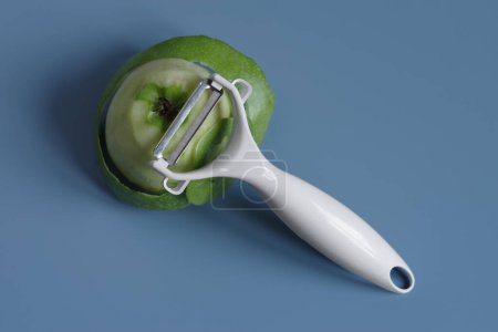 Téléchargez les photos : Couteau pour nettoyer les fruits et légumes avec pomme verte avec peau pelée sur fond bleu. - en image libre de droit