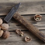 Whole and chopped walnuts next to a hammer on wood texture background.