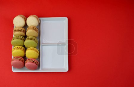 Photo for Multicolored macaroons in a white square plate on a bright red background. - Royalty Free Image