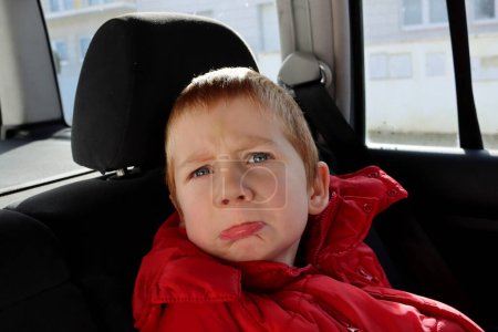Photo for The blond boy furrowed his brow and pursed his lips. A cranky five-year-old boy shows grimaces in the interior of the car. - Royalty Free Image