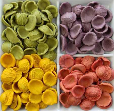 Pâtes Orecchiette non cuites de couleur italienne sèches en gros plan. Pâtes Orecchiette roses, lilas, jaunes et vertes. 