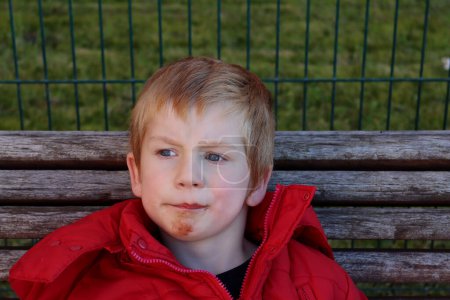 Photo for A blond boy with a dirty chin wrinkles his forehead and looks thoughtfully into the distance. Disgruntled five-year-old boy. - Royalty Free Image
