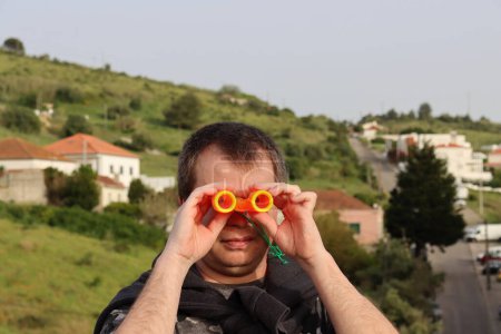 Téléchargez les photos : Un homme soyeux regarde à travers les jumelles orange pour enfants. - en image libre de droit