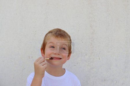 Téléchargez les photos : Un garçon joyeux mord des bâtons de pain sur le fond d'un mur de béton. Bonne enfance. - en image libre de droit