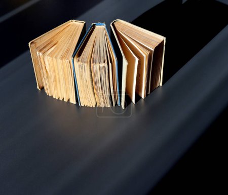 Semi-open hardcover books on a black background are arranged in a semicircle. Back to school. Side view