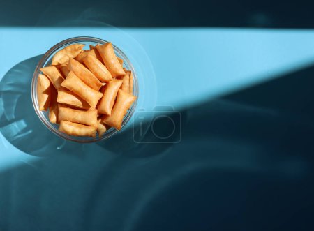 Crispy salt pads in a glass bowl on a blue background with shadow. Savory snack