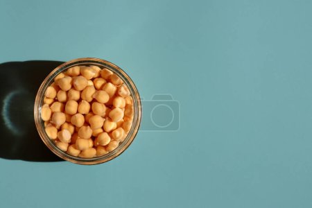 Soaking chickpeas in water to ferment cereals and neutralize phytic acid. Small glass jar with chickpeas filled with water close up on blue background
