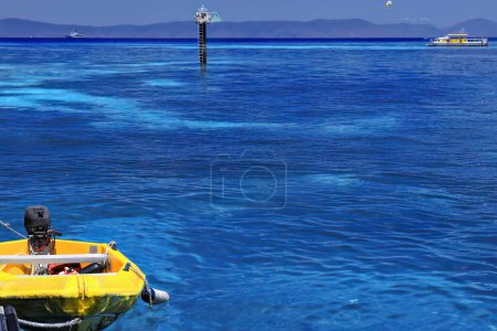 Téléchargez les photos : Yellow dinghy carried onboard a tourist motorboat moored at the Green Island-Wunyami jetty. Starboard marker beacon, hydrographic survey ship and snorkeling pontoon on background. Queensland-Australia - en image libre de droit