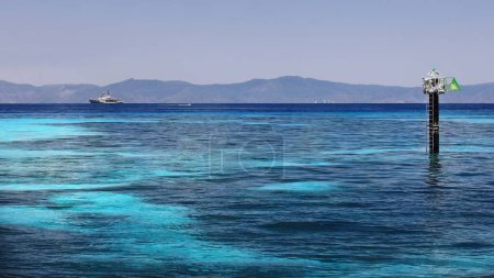 Foto de Starboard marker beacon, hydrographic survey ship and fast-going tourist motorboat seen from the Green Island-Wunyami mooring jetty, the shoreline north of Cairns as background. Queensland-Australia. - Imagen libre de derechos