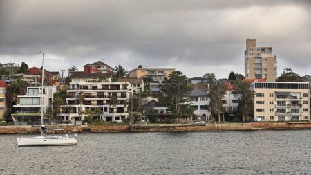 Foto de North Head peninsula harborside lined with waterfront residential buildings facing Manly Cove and moored sailboat as seen from the Manly to Sydney ferry starting its trip. Sydney Harbour-NSW-Australia - Imagen libre de derechos