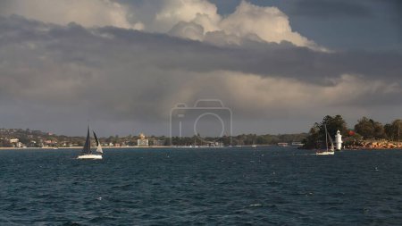 Téléchargez les photos : Voiliers de course naviguant dans les eaux sombres autour de Shark Island-Boowambillee par un après-midi nuageux avec Rose Bay à gauche et Shark Island Light à droite. Port de Sydney-NSW-Australie. - en image libre de droit