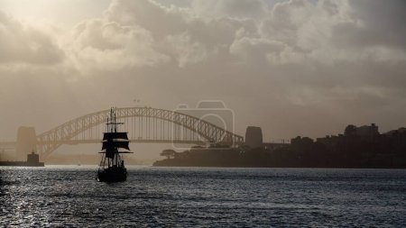 Téléchargez les photos : Silhouette noire d'un barquentin traditionnel ou d'une goélette barque grand navire naviguant vers l'ouest dans les eaux de Port Jackson dans un après-midi très brumeux Harbour Bridge en arrière-plan. Sydney-NSW-Australie - en image libre de droit