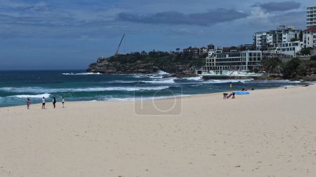 Photo for Southwards view over Bondi Beach to South Bondi Headland and the ocean swimming pool with tourist beachgoers, while surfers try to ride the waves. Sydney-NSW-Australia. INCIDENTAL PEOPLE IN THE IMAGE. - Royalty Free Image
