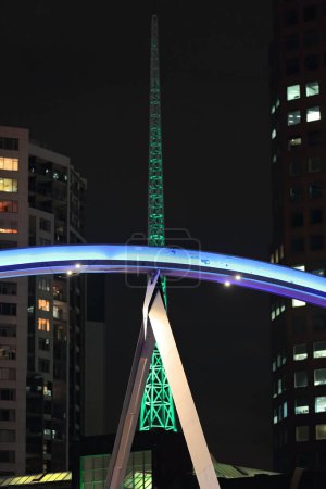 Photo for Night view southeastwards from the Flinders Walk along the Yarra river north-right bank to the illuminated Southbank Pedestrian Bridge backed by a 1996 built green-lit spire. Melbourne-VIC-Australia. - Royalty Free Image