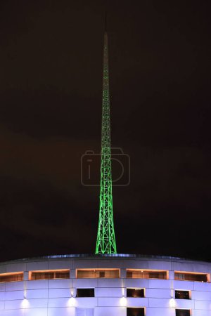 Photo for Night view from Flinders Walk along the Yarra river north-right bank to a modern round building and a green-illuminated tall spire in the city Arts Precinct, Southbank suburb. Melbourne-VIC-Australia. - Royalty Free Image