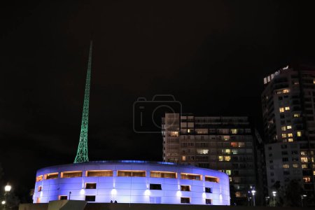 Photo for Night view from Flinders Walk along the Yarra river north-right bank to a round building, tall apartment towers and a green-lit spire in the Arts Precinct, Southbank suburb. Melbourne-VIC-Australia. - Royalty Free Image