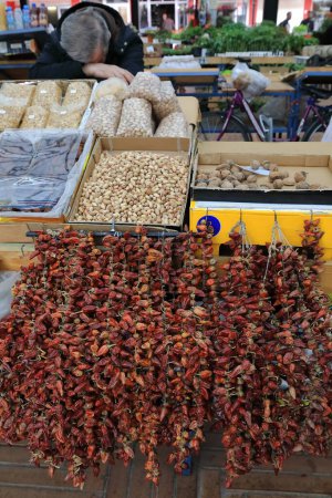 Téléchargez les photos : Vendeur de sieste dans un étal de marché vendant dans des sacs en plastique-boîtes en carton un hodgepodge de cacahuètes, figues, pistaches, noix et ristras de piment sec au Pazari i Ri-New Bazaar. Tirana-Albanie - en image libre de droit