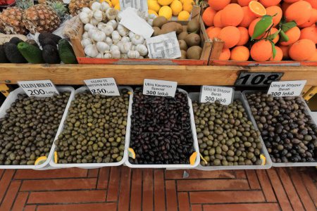 Téléchargez les photos : Olives de table de plusieurs types et divers fruits ananas-avocat-citron-kiwi-orange- à vendre dans des conteneurs en plastique et des boîtes en bois dans un étal de marché du Pazari i Ri-New Bazaar. Tirana-Albanie. - en image libre de droit