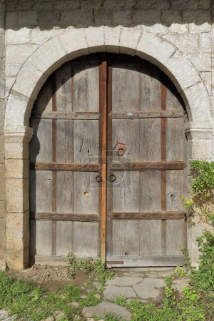 Téléchargez les photos : Porte en bois taillée dans le mur de maçonnerie de pierre d'une maison de la rue Rruga Kristaq Tutulani du district de Gorica, déchiquetée, à charnière, incolore, à arche ronde, à rebord et à corniche. Berat-Albanie. - en image libre de droit