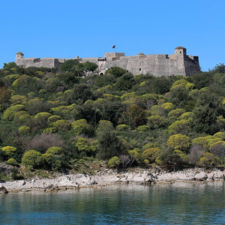 Vue vers l'ouest depuis le continent de la baie de Porto Palerme jusqu'au château Ali Pacha de Tepelene reconstruit en 1804 sur une ancienne forteresse vénitienne de la fin du XV-début du XVI siècle au sommet d'une péninsule rocheuse. Himare-Albanie.