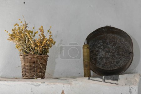 Téléchargez les photos : Décor intérieur : sidérite sèche ou fleurs de morelle dans un panier en osier tissé à la main, vieux moulin à café en laiton manuel de style turc et plaque de cuisson en fer, le tout dans une maison ottomane du début des années 1700. Gjirokaster-Albanie. - en image libre de droit