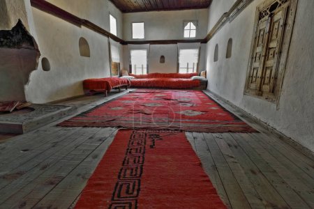 Téléchargez les photos : Au début des années 1700, la maison ottomane salon dans son architecture et son décor d'origine : tapis kilim tissés à la main de couleur rouge, divan et canapé avec couverture en molleton teint en rouge, immense cheminée. Gjirokaster-Albanie. - en image libre de droit