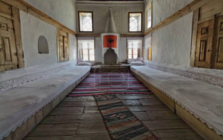 Téléchargez les photos : Maison ottomane du début des années 1700 salon dans son architecture et son décor d'origine : tapis kilim tissés à la main de couleur mamie, longs autocars longitudinaux recouverts de tissu blanc, immense cheminée. Gjirokaster-Albanie. - en image libre de droit