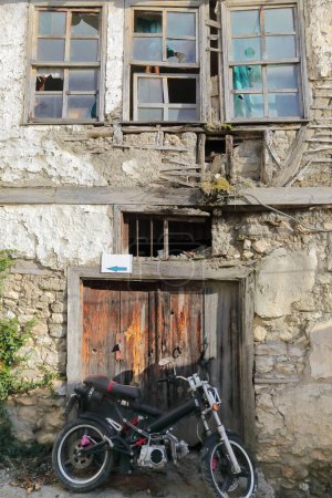 Foto de Moto submarino estacionado en la puerta de madera cerrada, astillada y pelada de una antigua casa tradicional abandonada y deteriorada en un callejón del barrio Varos-Casco Antiguo. Ohrid-Macedonia del Norte. - Imagen libre de derechos