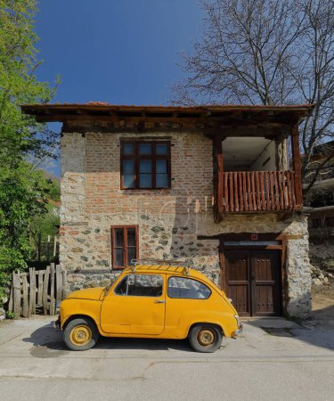 Foto de El clásico automóvil amarillo anaranjado, el llamado Fikjo de la era comunista yugoslava, se detuvo frente a una casa local al principio del camino que iba a los manantiales locales. Vevcani-Macedonia del Norte. - Imagen libre de derechos